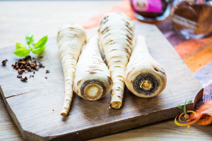 Three Harris Model parsnips on a wooden cutting board with spices and herbs nearby